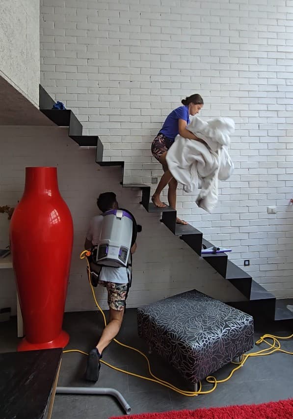 Two Qtana team members vacuuming and carrying fresh linens on a staircase